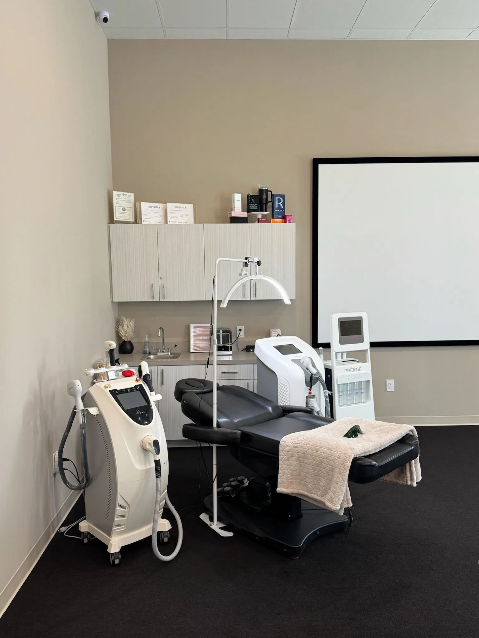 Medical clinic room with treatment devices, cabinets, exam chair, and large projection screen.