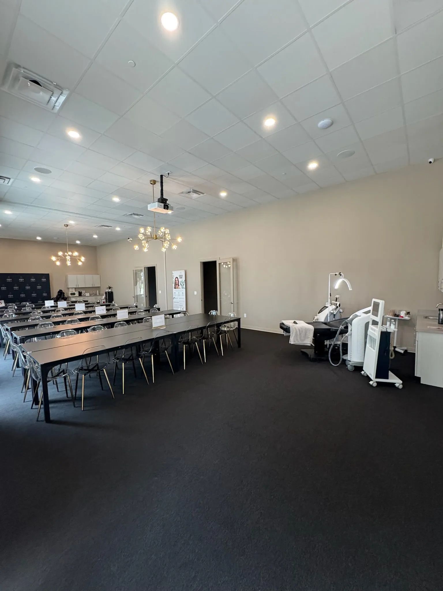 Empty conference room with long tables, black chairs, and white exercise equipment on a dark carpeted floor