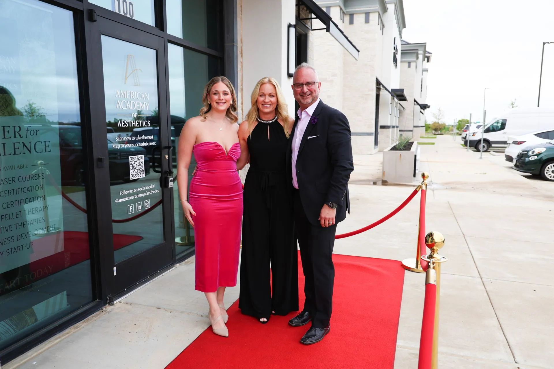 Three people posing on a red carpet outside a building entrance.