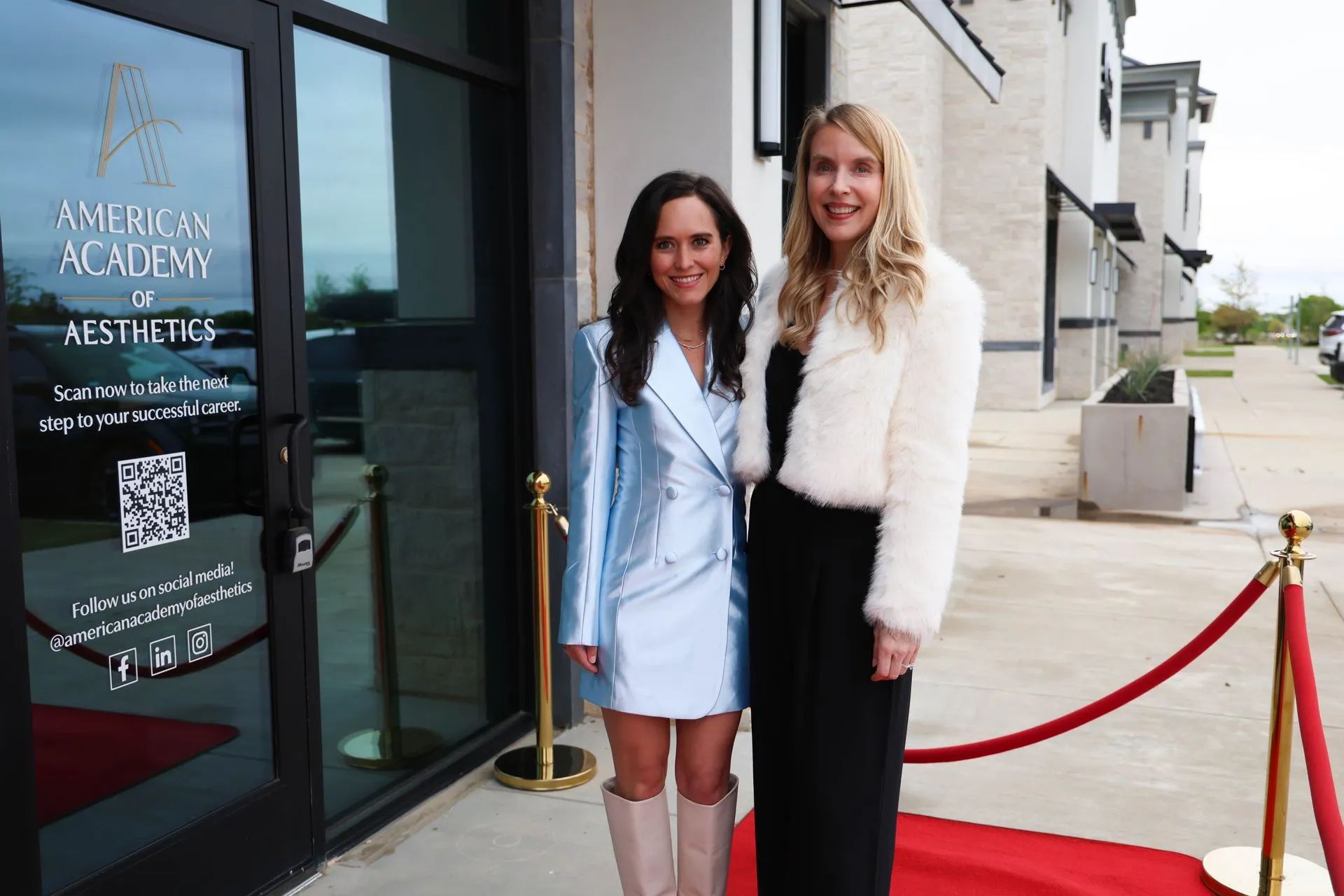 Two women posing outside a storefront with a red carpet and velvet ropes