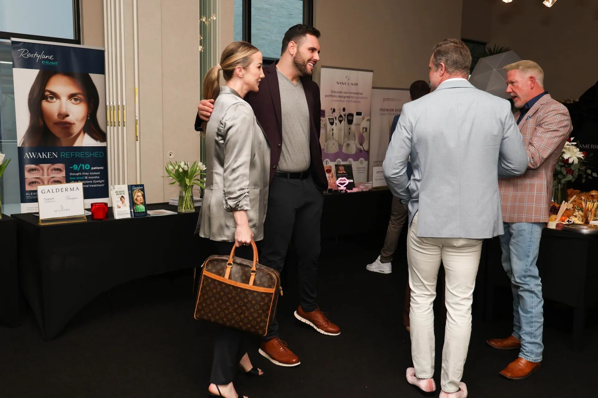 Small networking group chatting at an indoor event beside a display table and poster