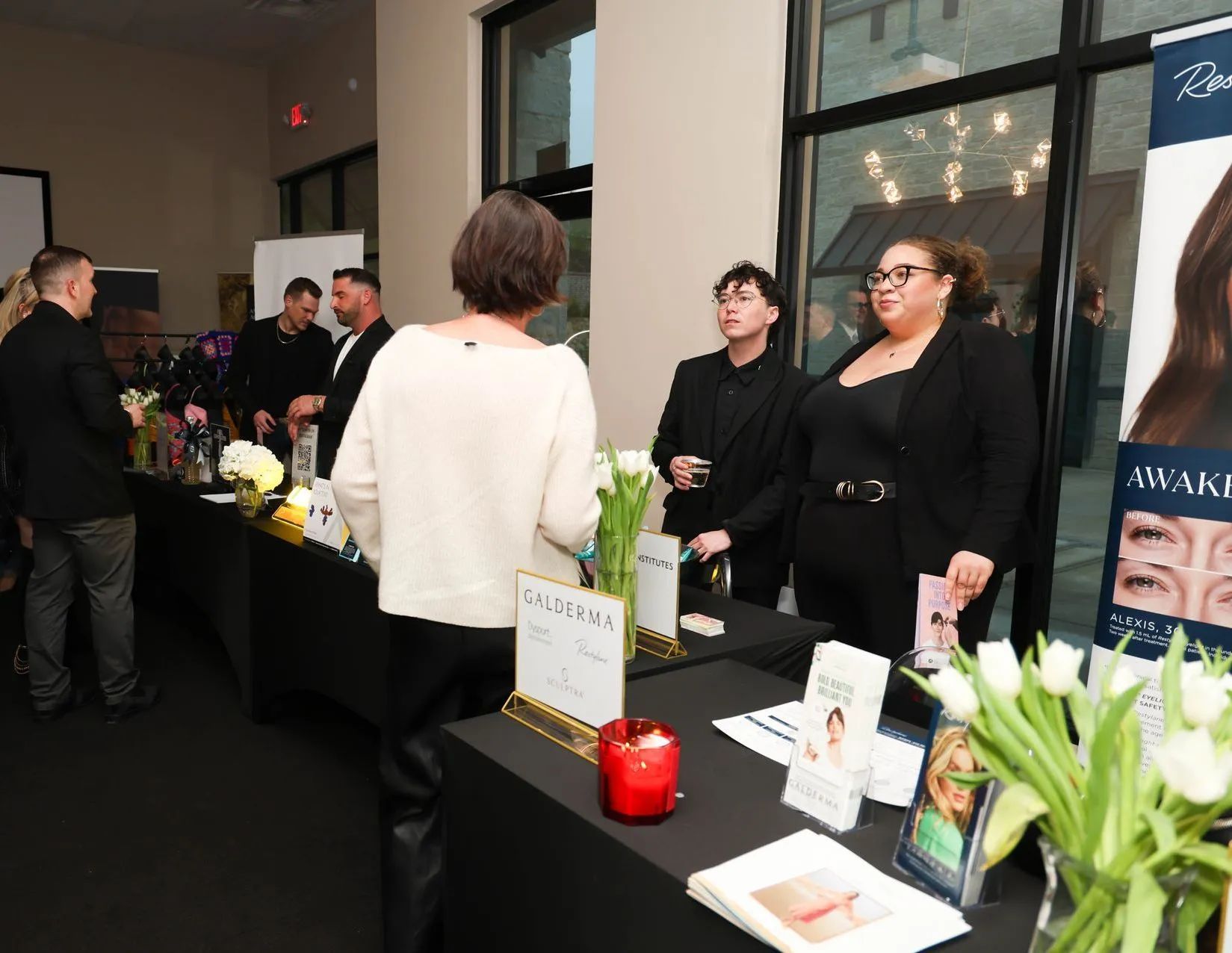 People at a vendor table in a lobby, with flowers, candles, and product displays on black tablecloths.