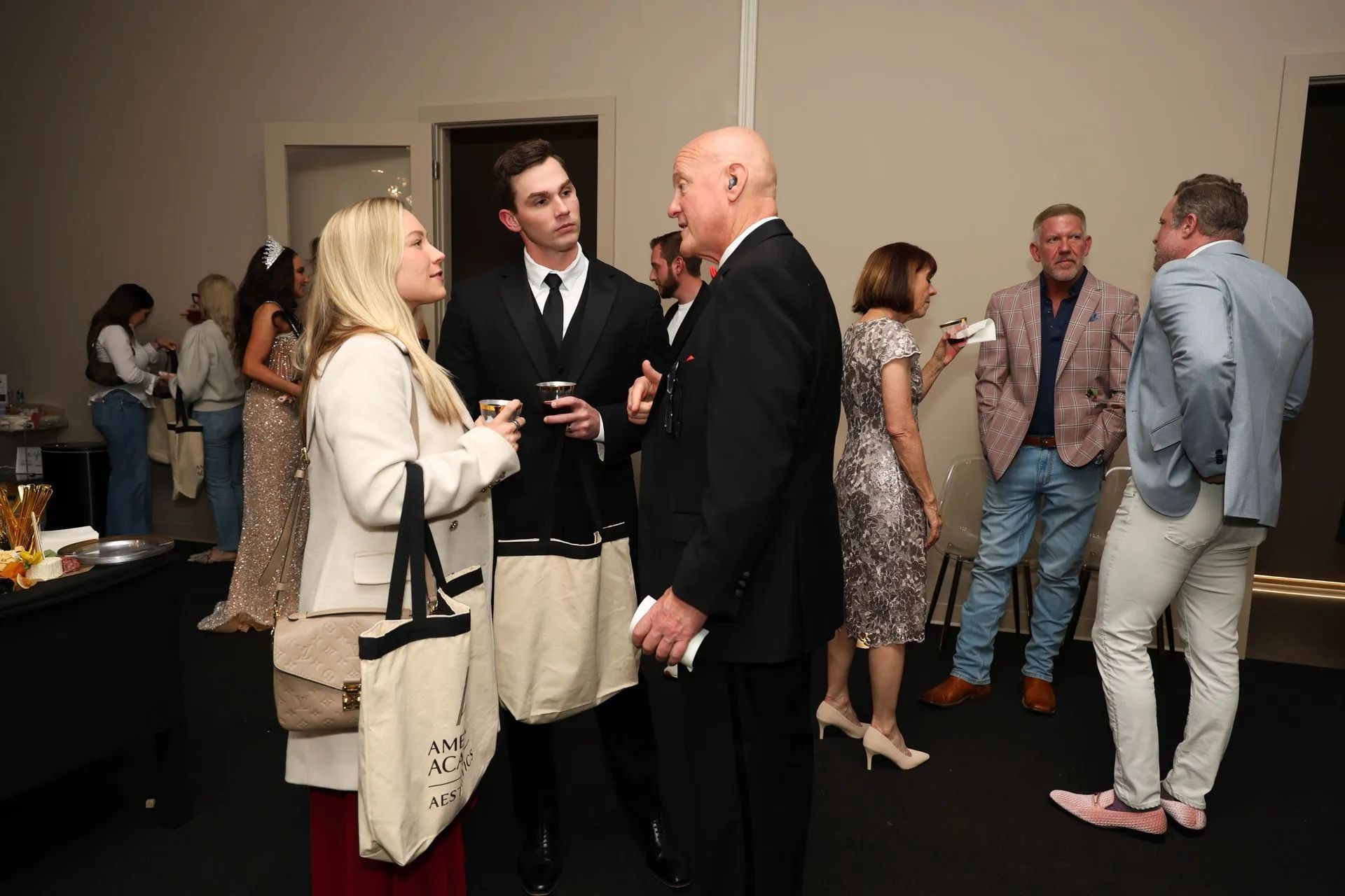 People mingling at an indoor networking event, with guests in suits and dresses conversing near a buffet.