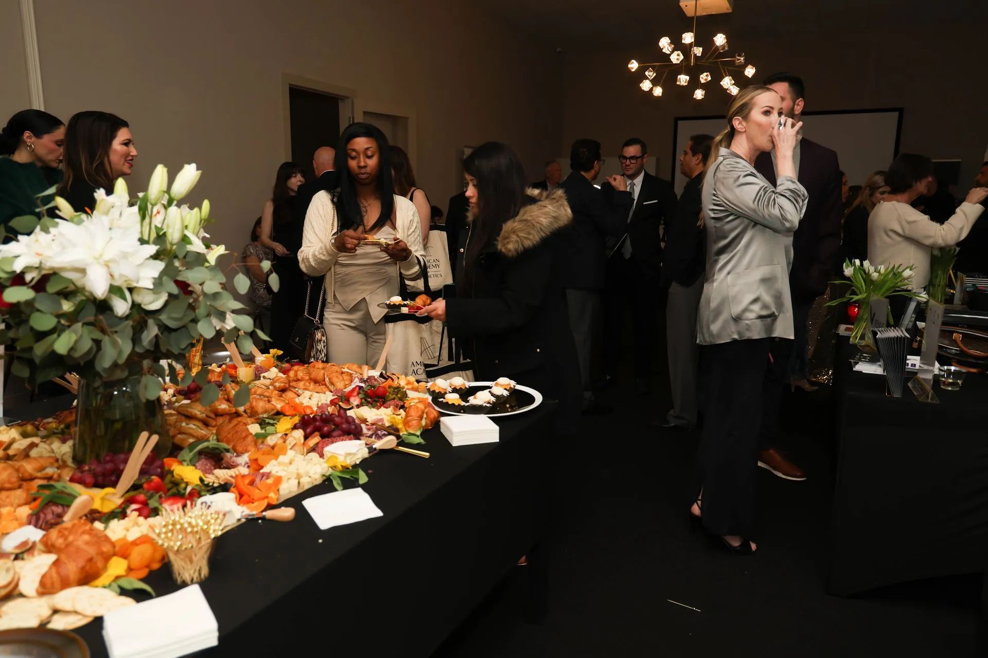 Catering table with food and flowers at a formal indoor reception, guests mingling in the background