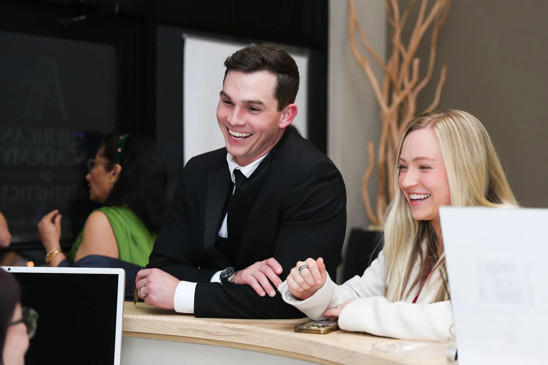 Two smiling coworkers in business attire leaning over a table in a modern office setting