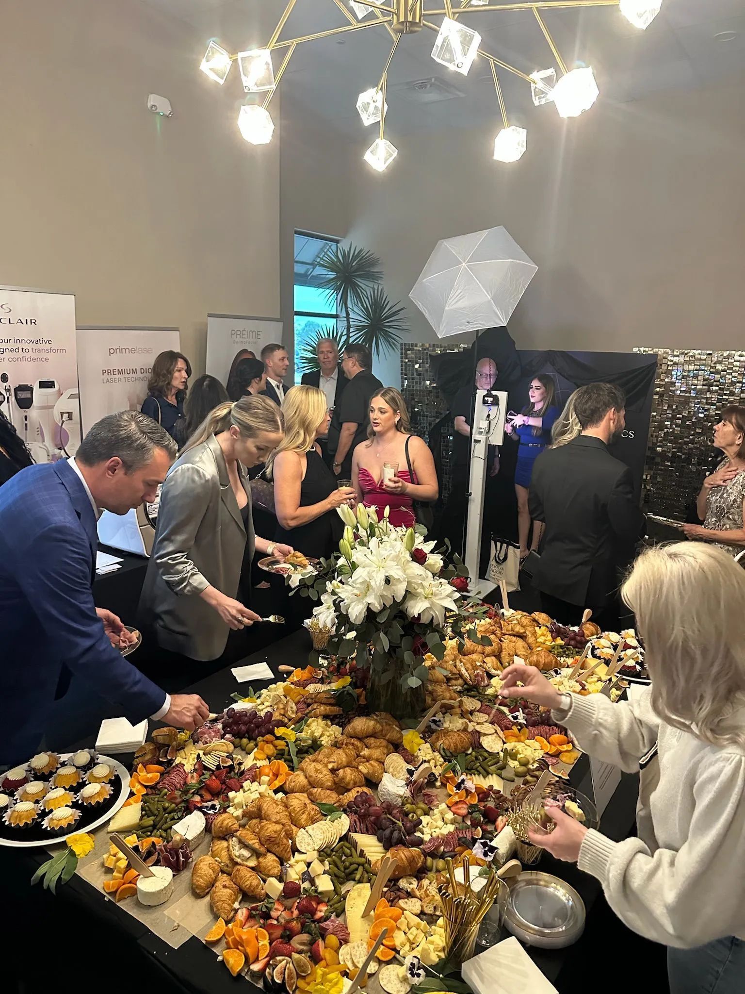 Guests mingle around a floral buffet table at an indoor cocktail reception under warm hanging lights