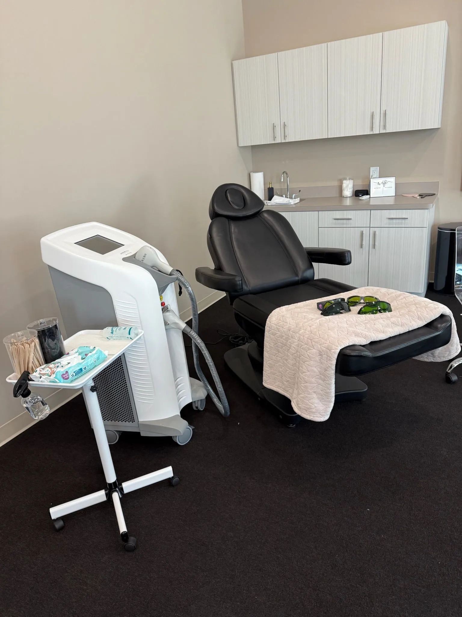Spa treatment room with black chair, facial machine, and cabinet