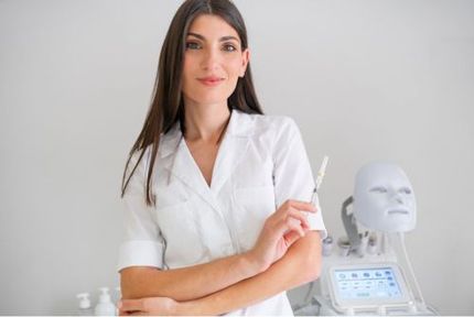 Professional in white coat standing beside a medical training mannequin and device, holding a pen