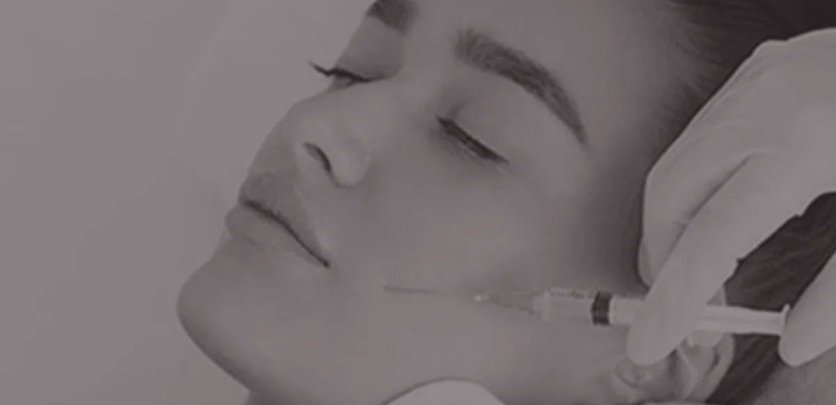 Close-up of a person’s face with a medical syringe near the cheek during an injection.
