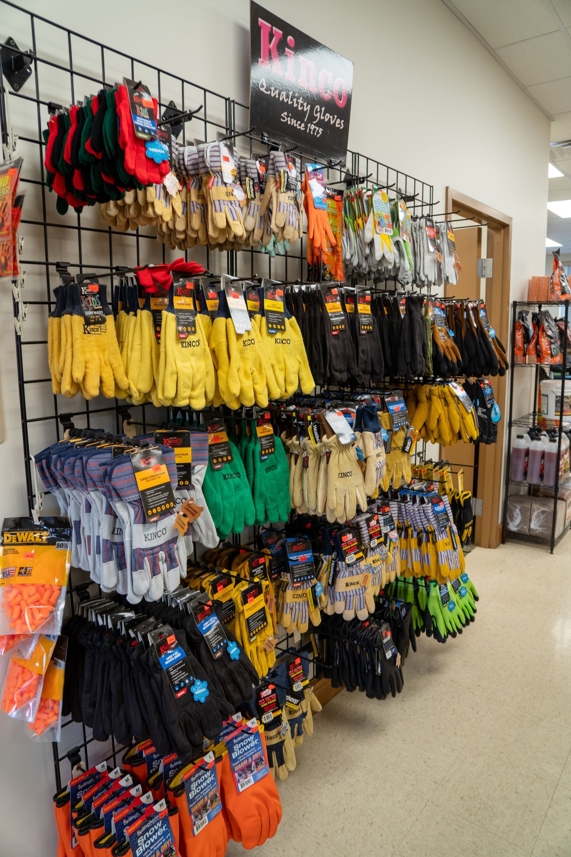 Gloves of various colors on display in a store, hanging on a black grid shelf.