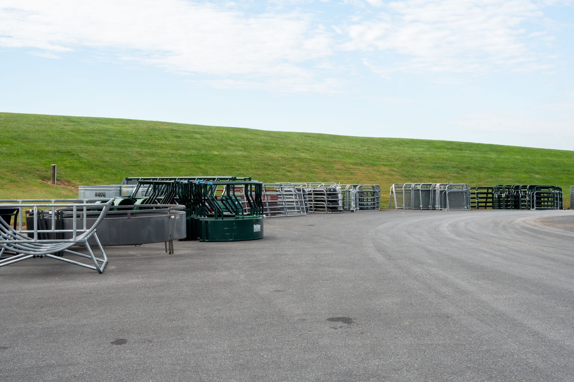 Metal scaffolding and barriers on a paved area, green hill in the background, under a cloudy sky.