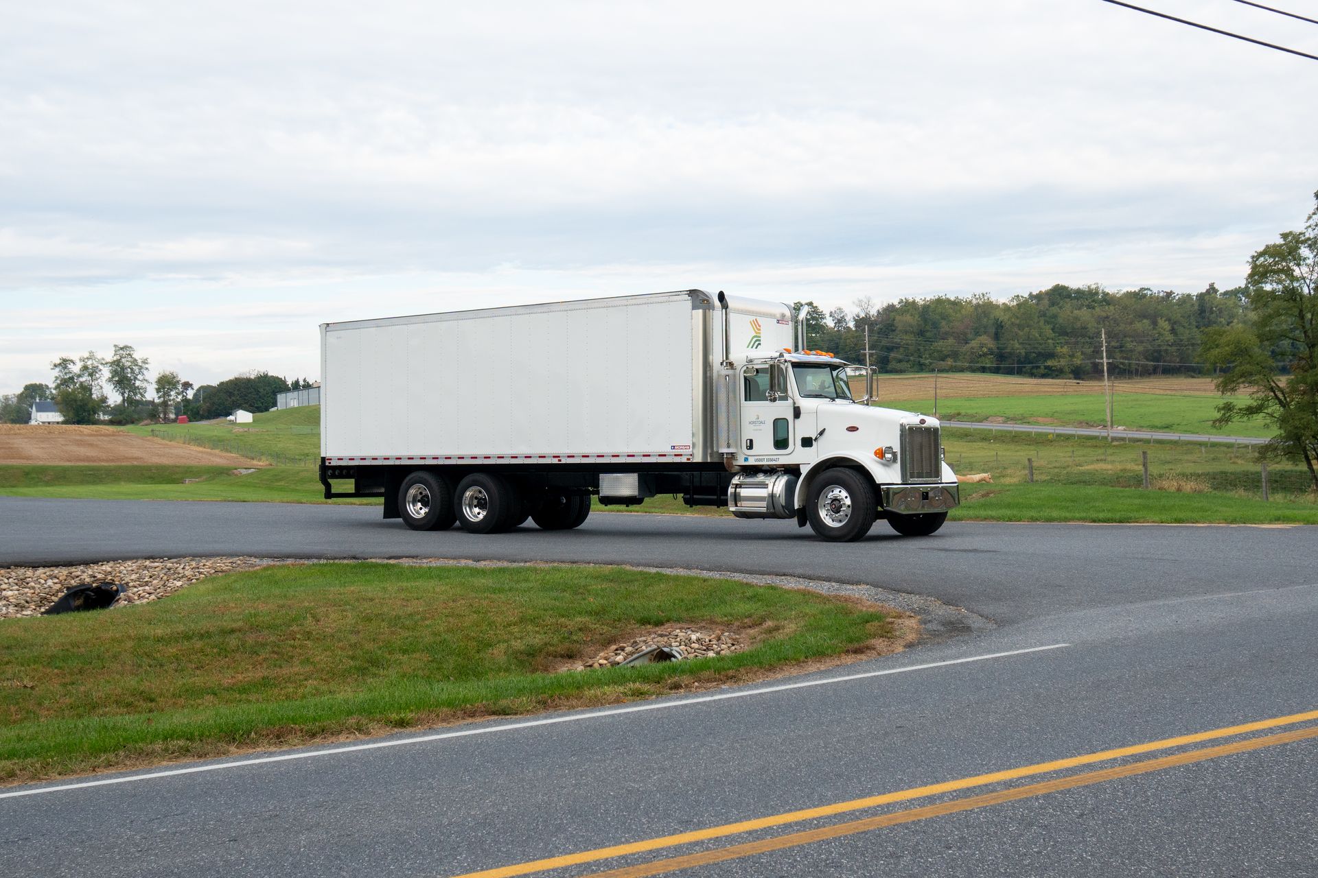 White semi-truck with a cargo container driving around a bend in a rural road.