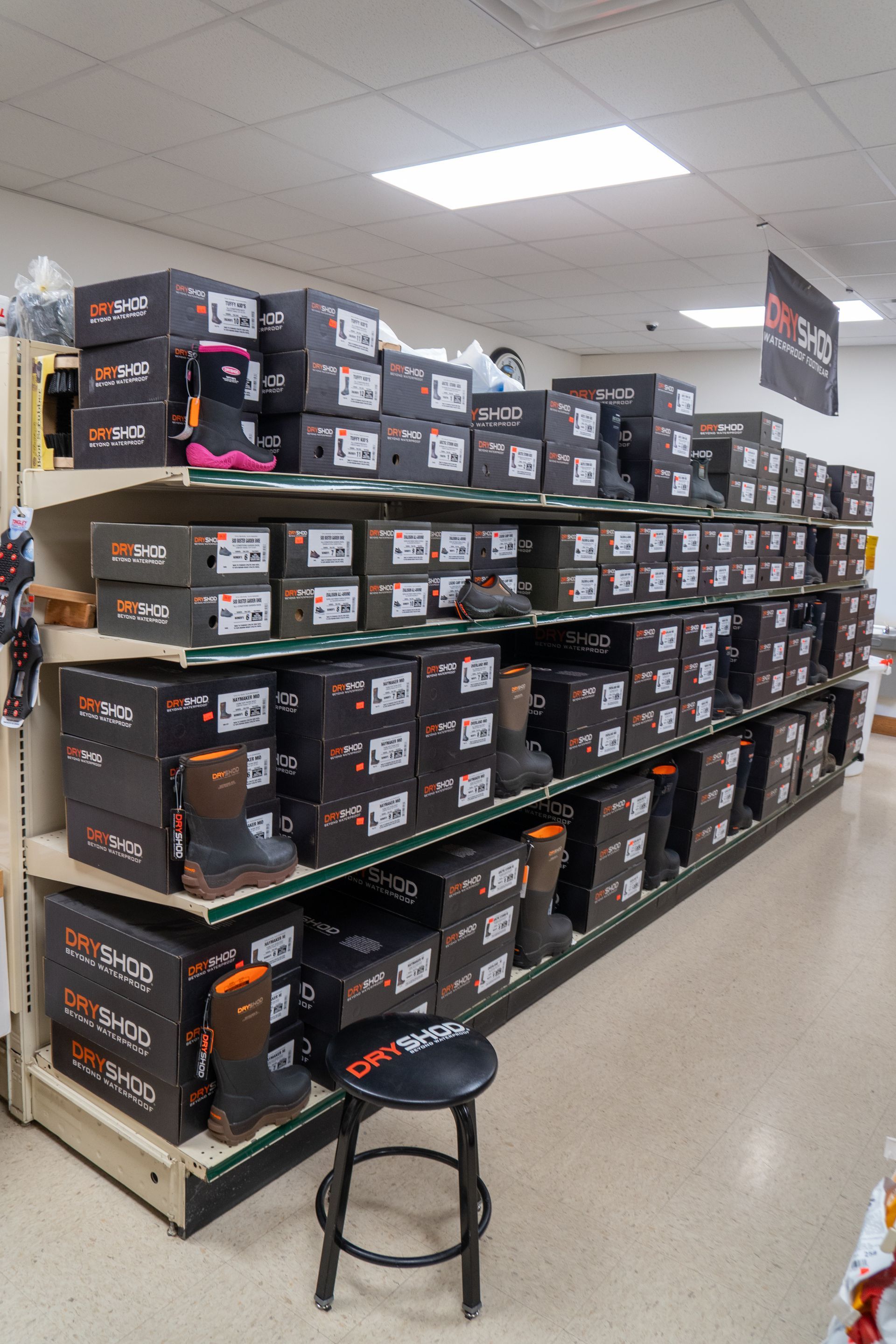 Shelves stocked with boxed work boots in a store; a stool sits in the aisle.
