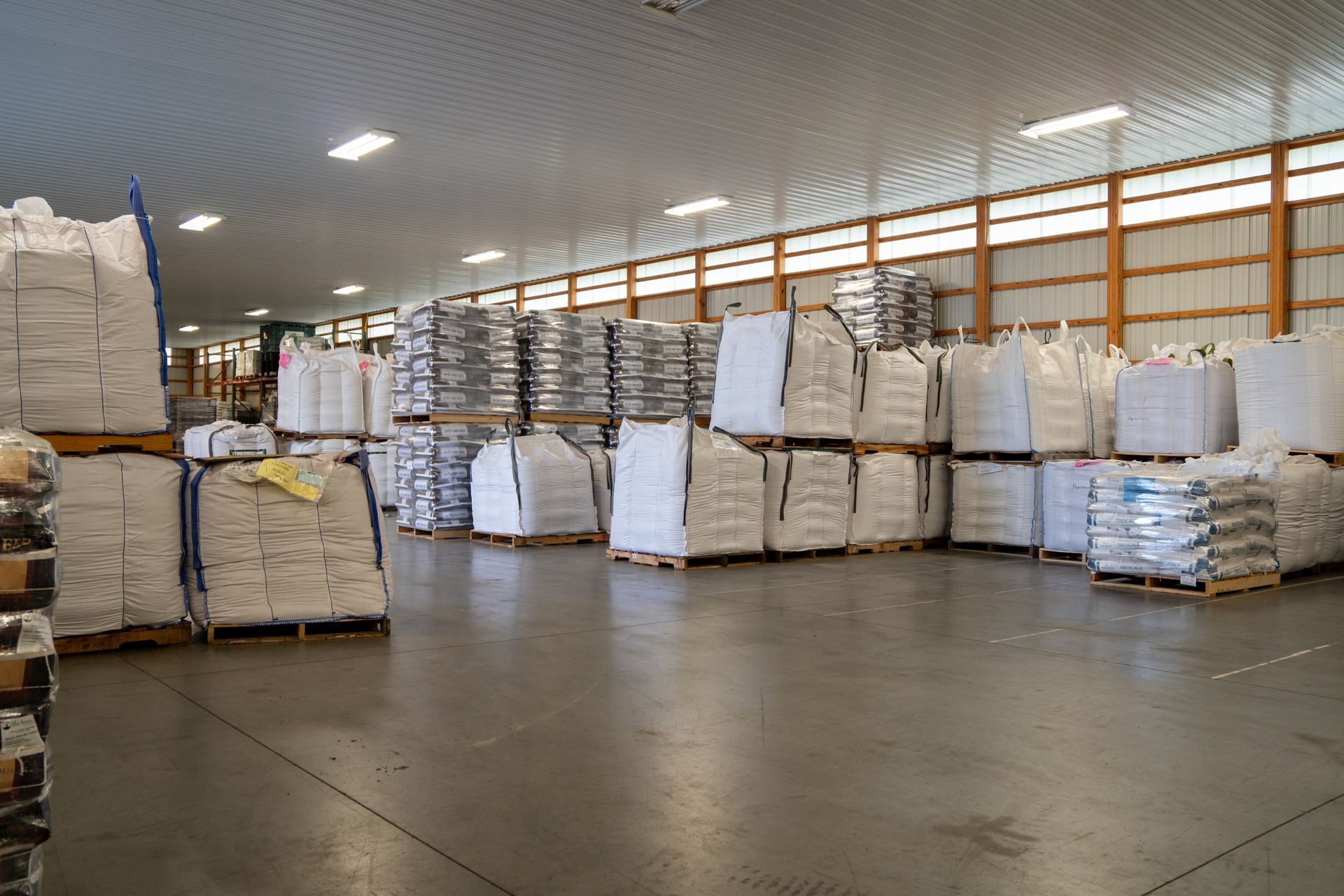 Large warehouse with stacks of white bags on pallets, under bright fluorescent lights.