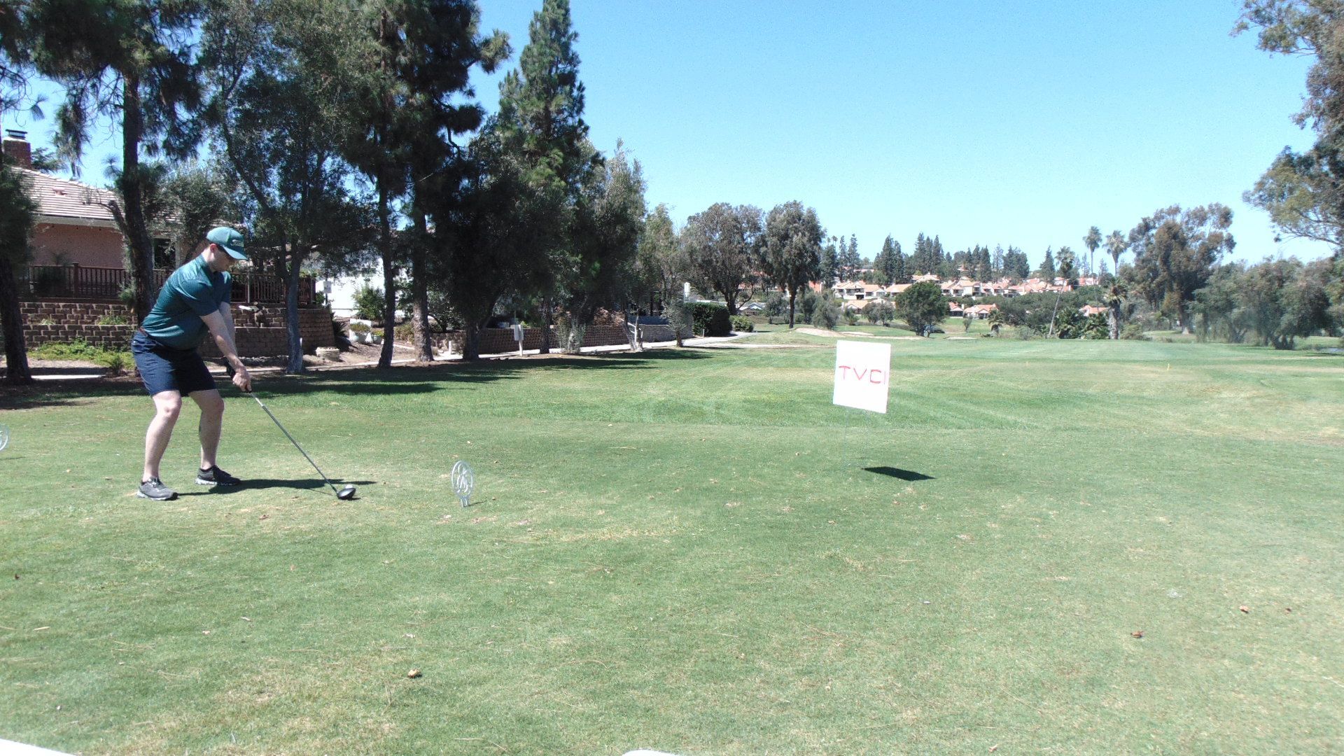 Person swinging a golf club on a sunny course near a white sign