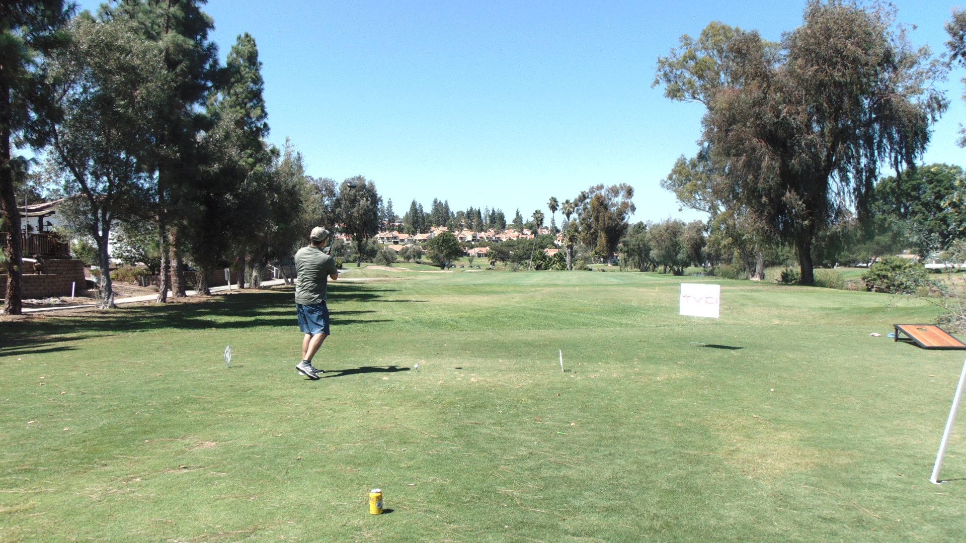 Person playing golf on a green course under a clear blue sky.