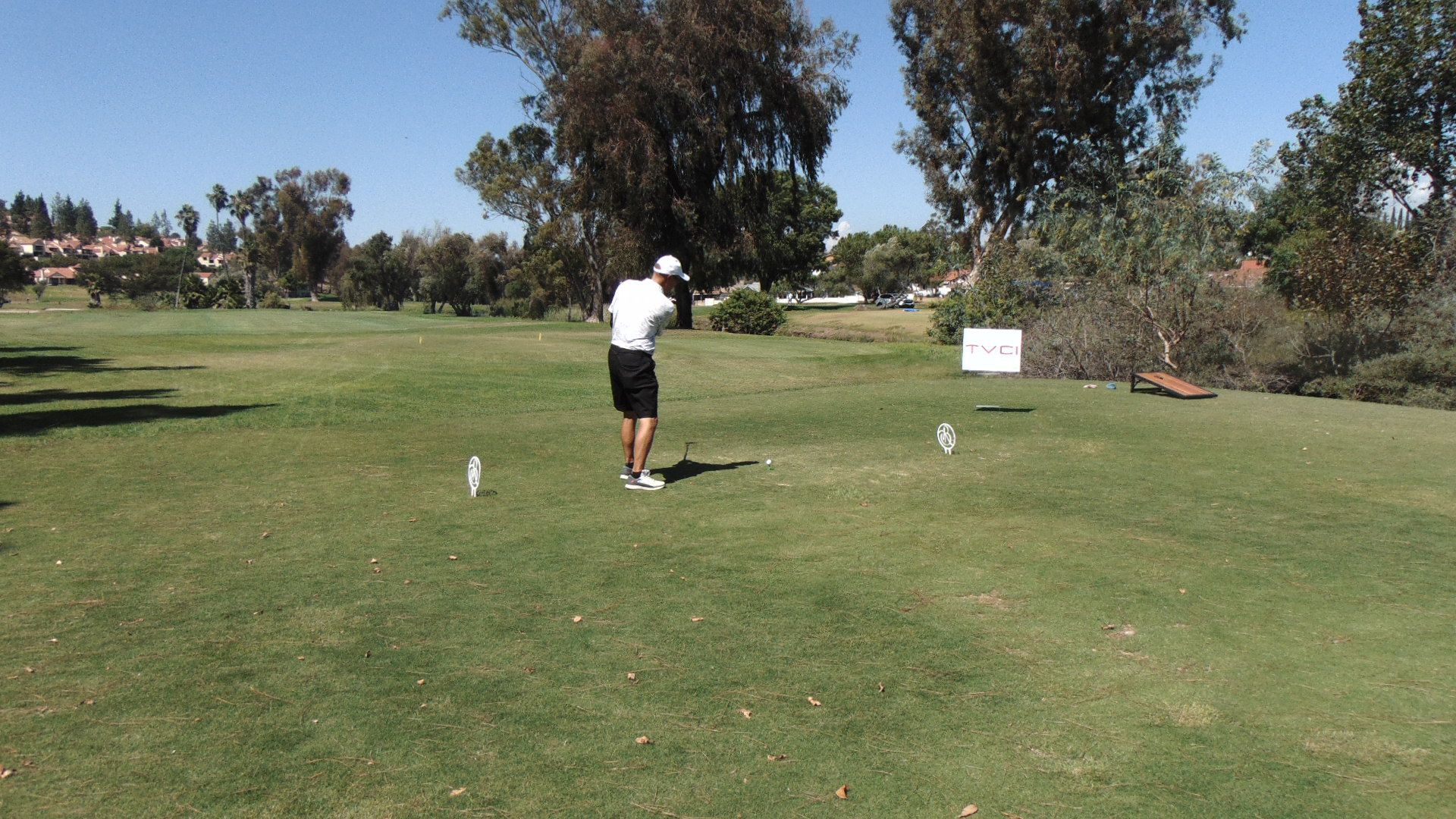 Golfer in white shirt and black shorts preparing to tee off on a sunny golf course