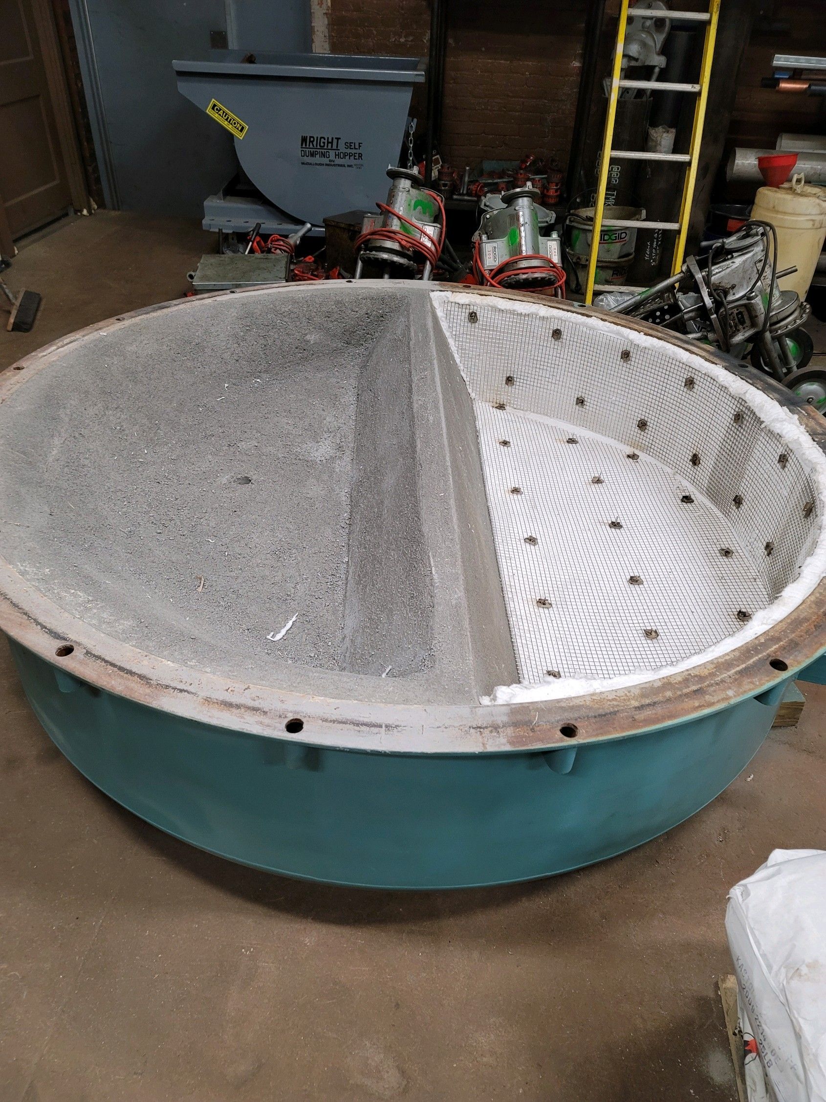 A large blue bowl is sitting on the floor in a room next to a ladder.
