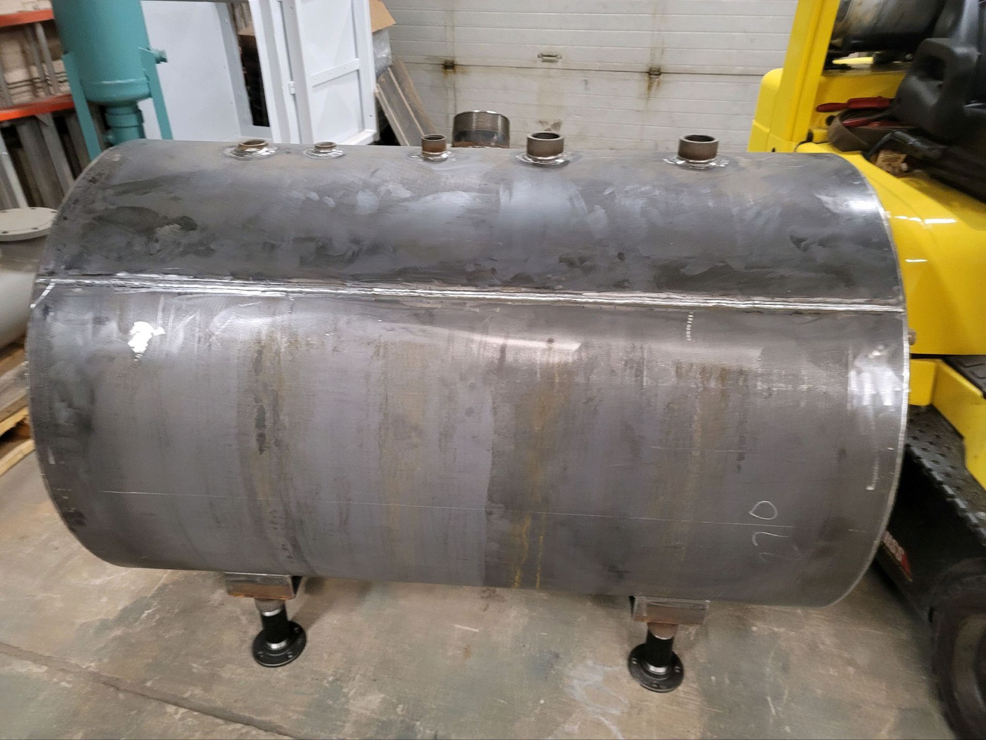 A large metal cylinder is sitting next to a yellow forklift