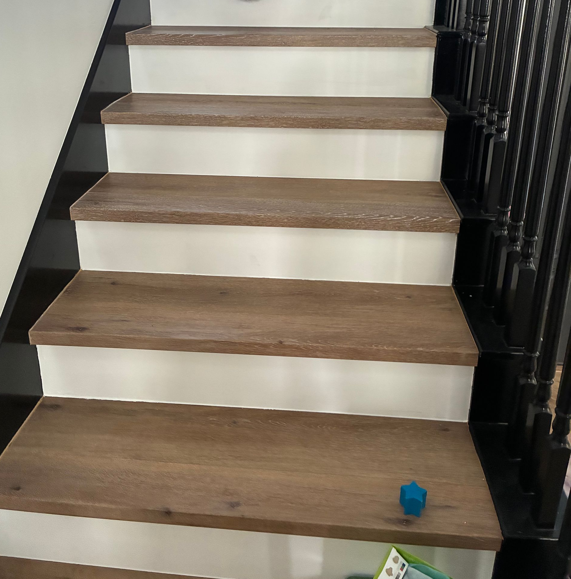 A staircase with brown wood treads and white risers, featuring a dark wood stringer and black metal balusters.