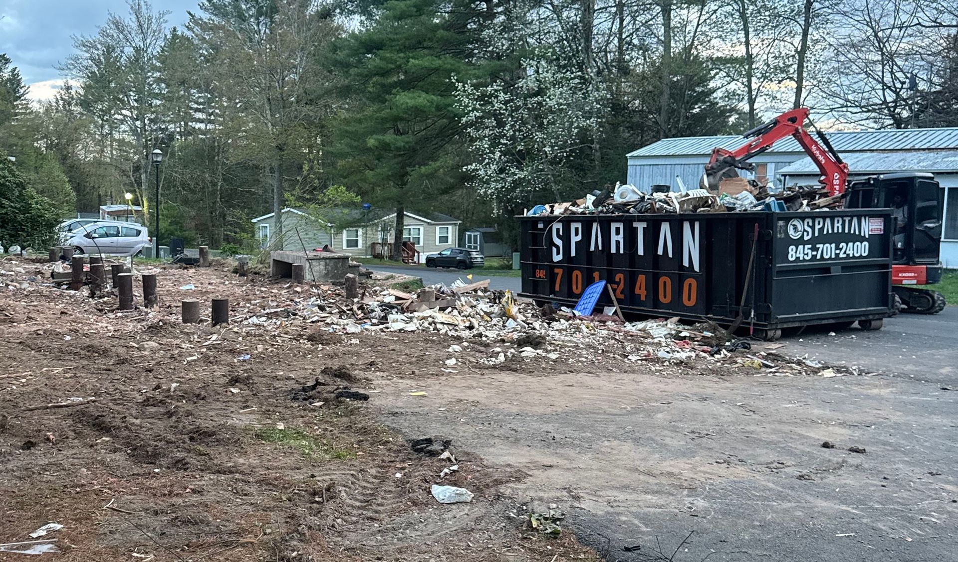 Demolition site with a Spartan dumpster and excavator, debris scattered.