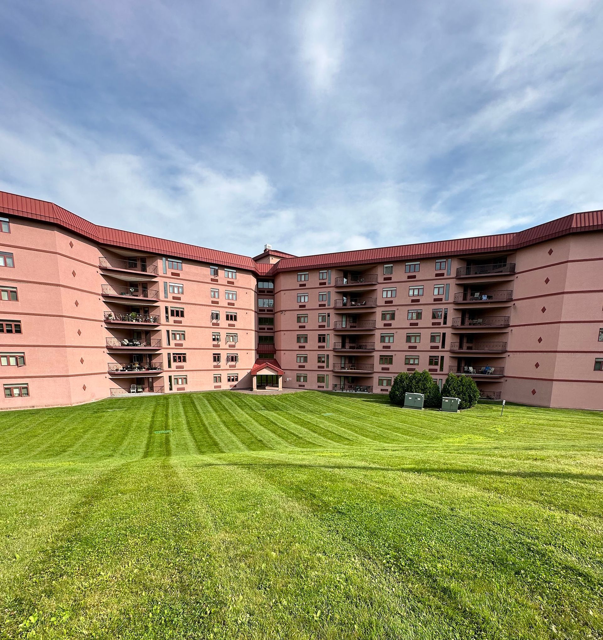 Pink apartment building with red roof, overlooking a green lawn under a blue sky.