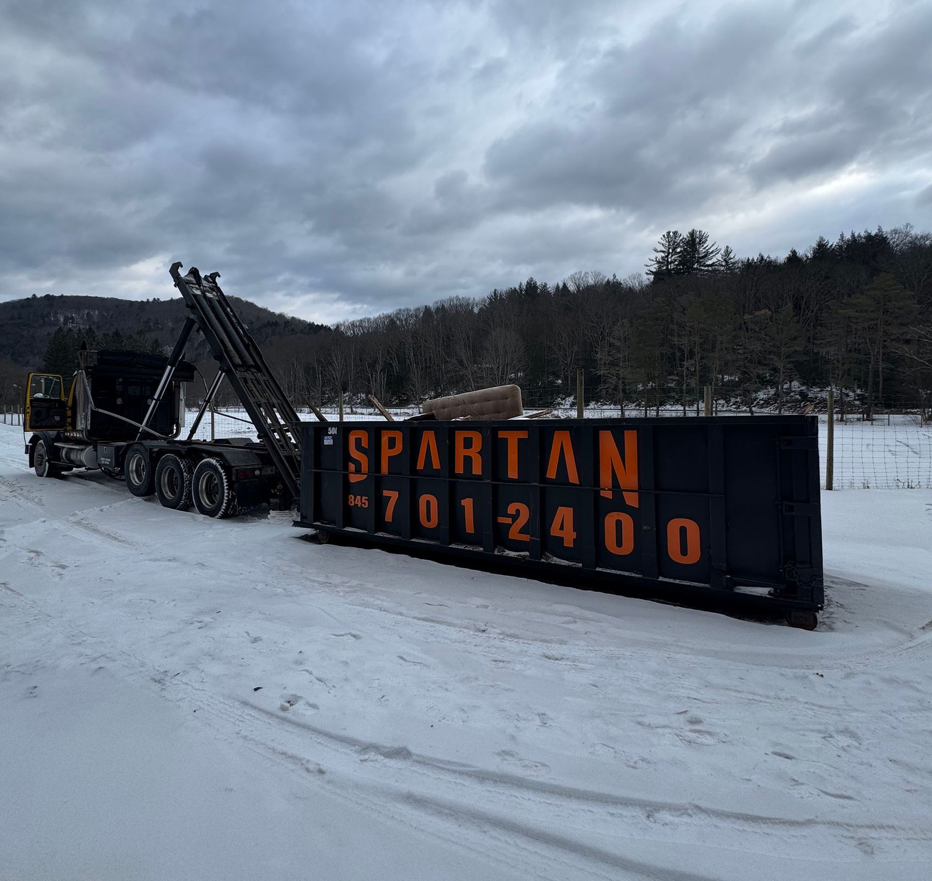 Black Spartan dumpster in snowy setting with truck; phone number visible.