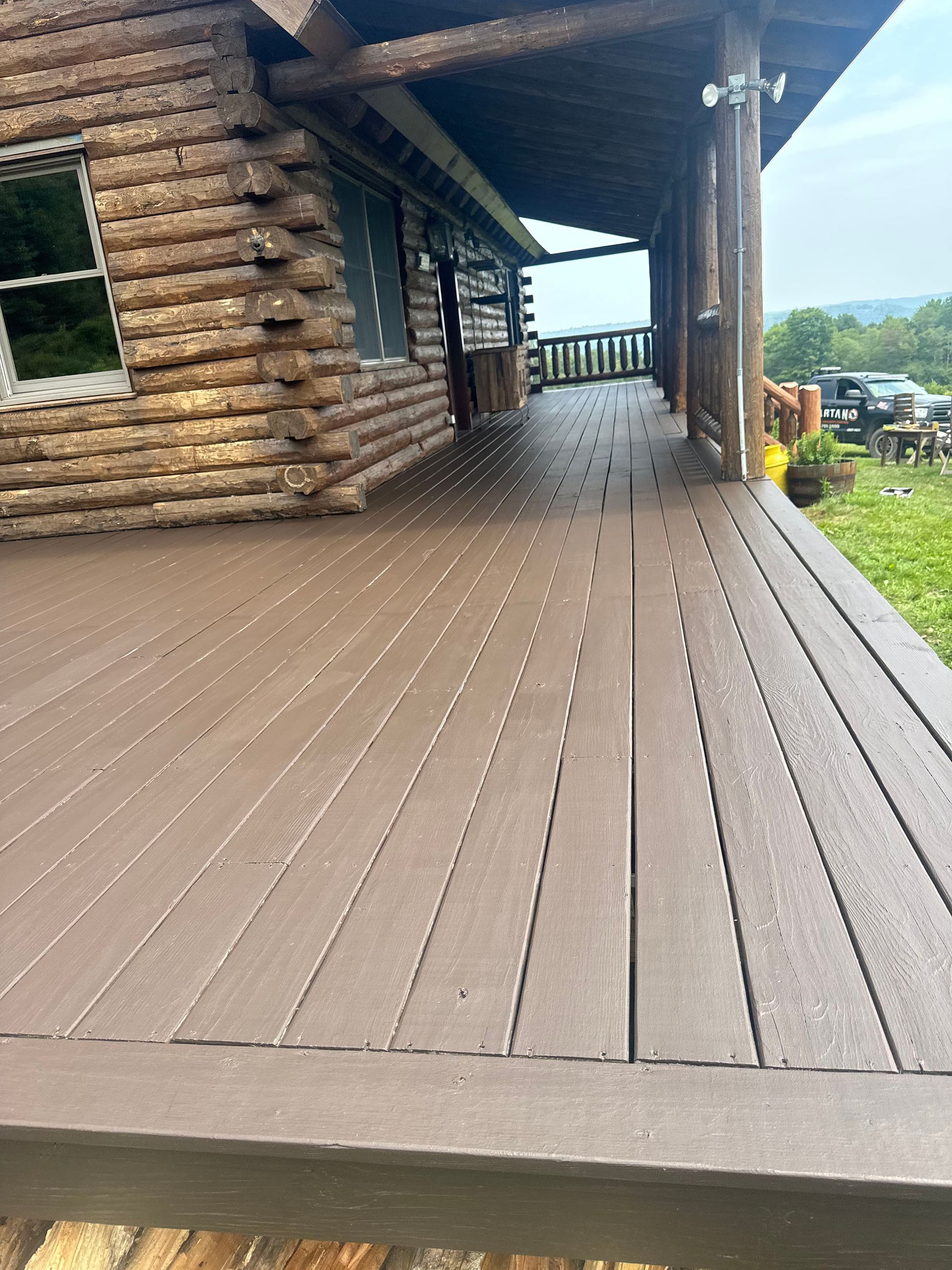Brown wooden deck extending from a log cabin. Covered porch and outdoor setting.