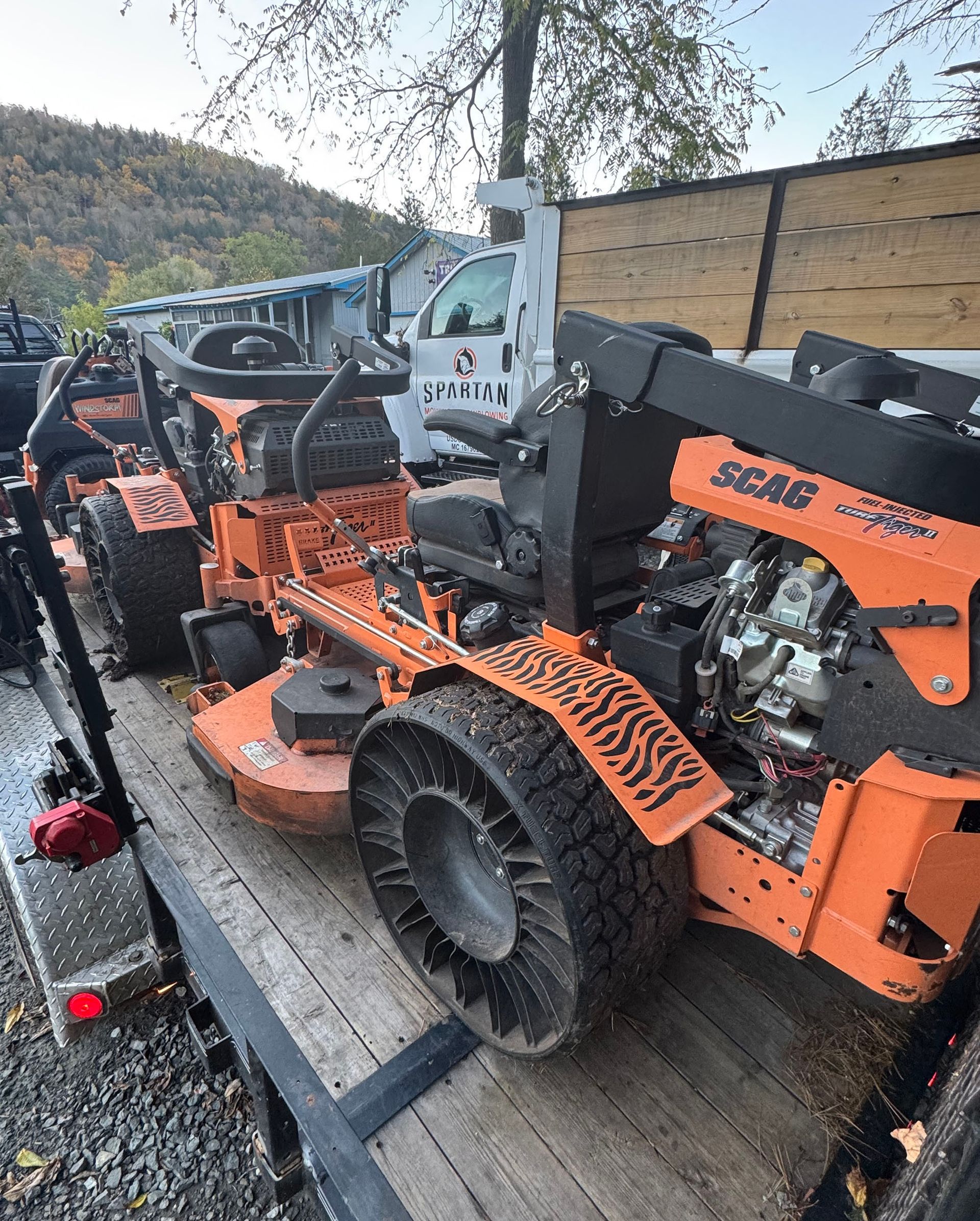 Two orange SCAG mowers on a trailer, ready for transport.