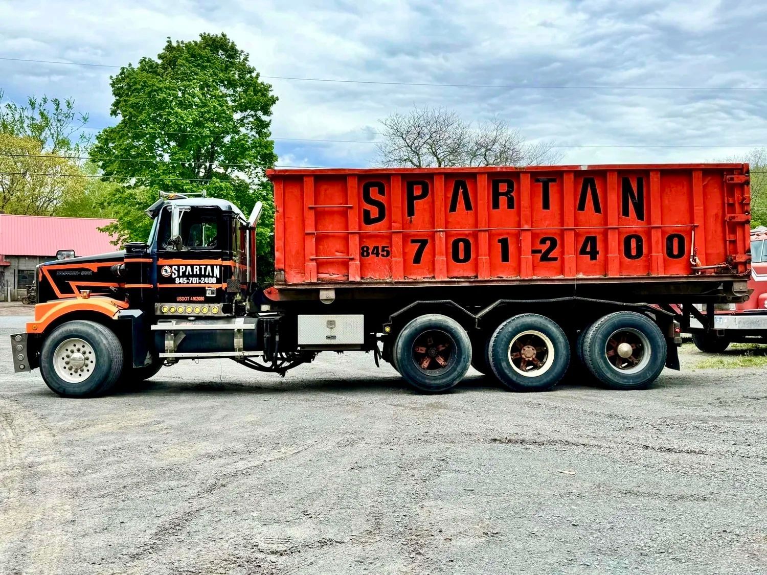 Orange Spartan dump truck with black cab parked on gravel, near a building.