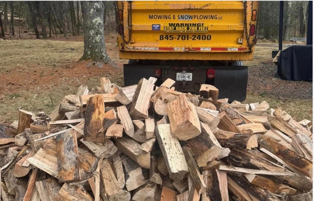 Pile of firewood in front of a yellow dump truck.