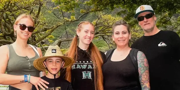 Five people posing outdoors under trees, smiling at the camera.