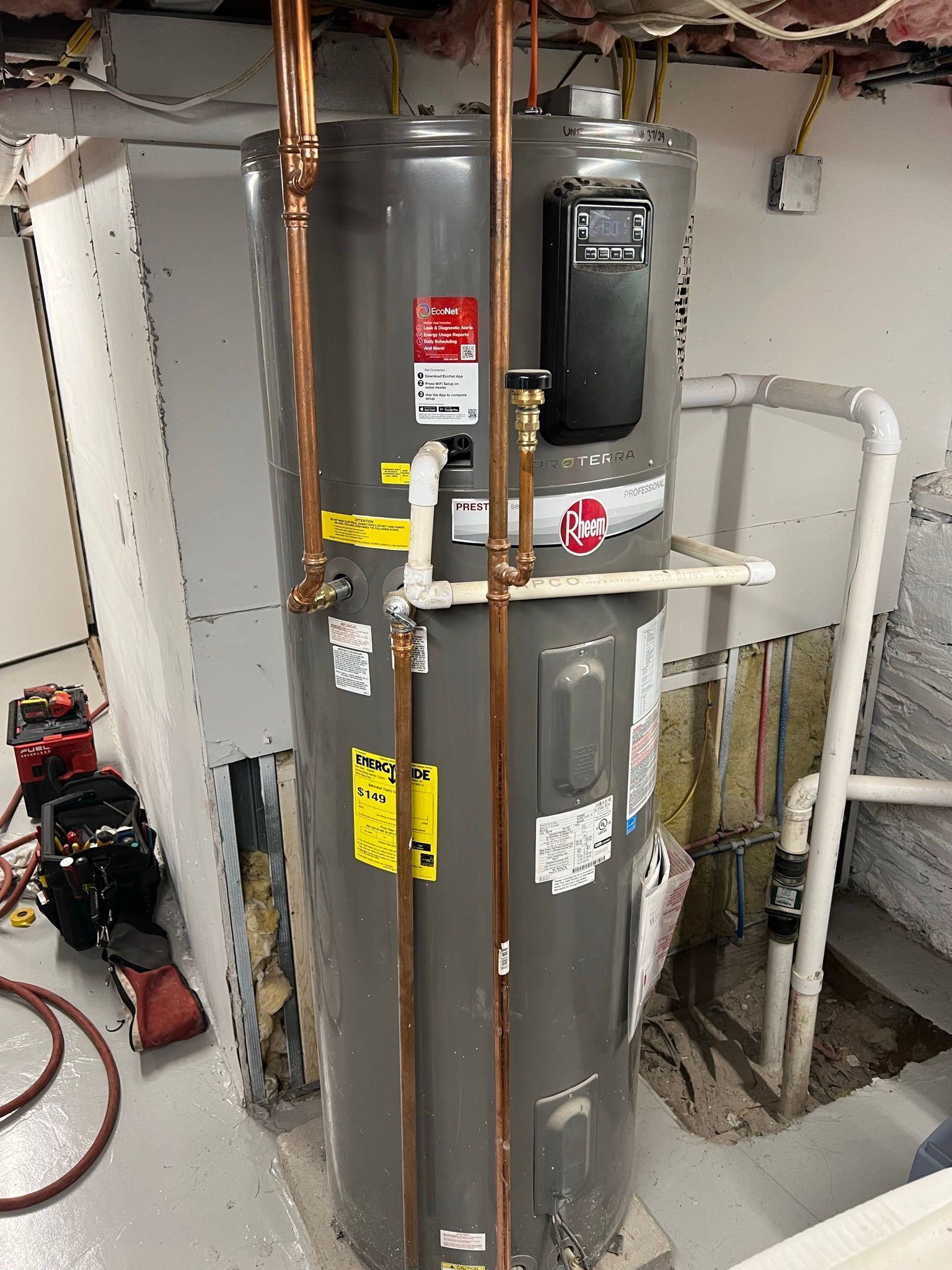 a gray water heater is sitting in a basement next to copper pipes