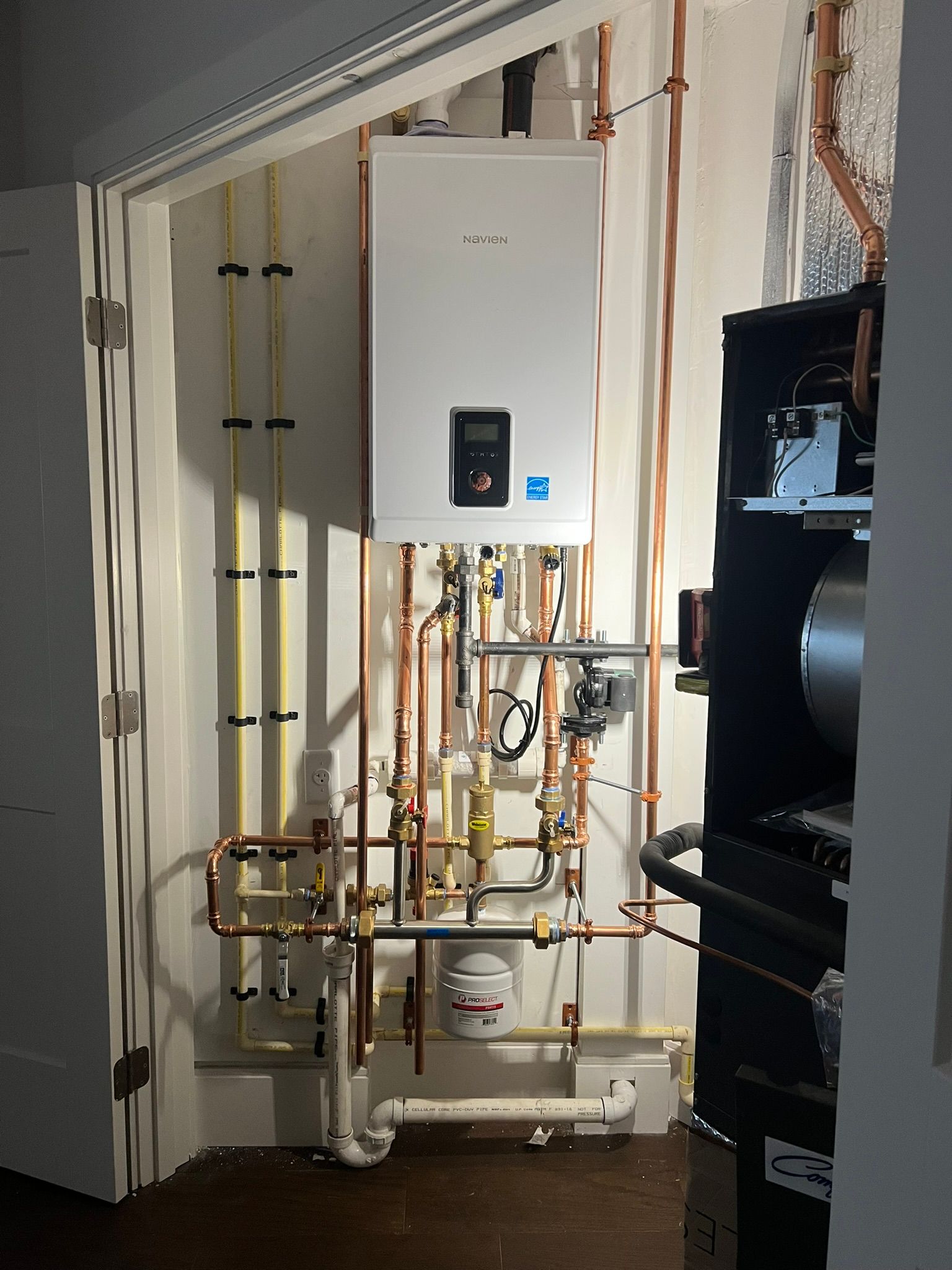 a white water heater is mounted on a wall next to copper pipes