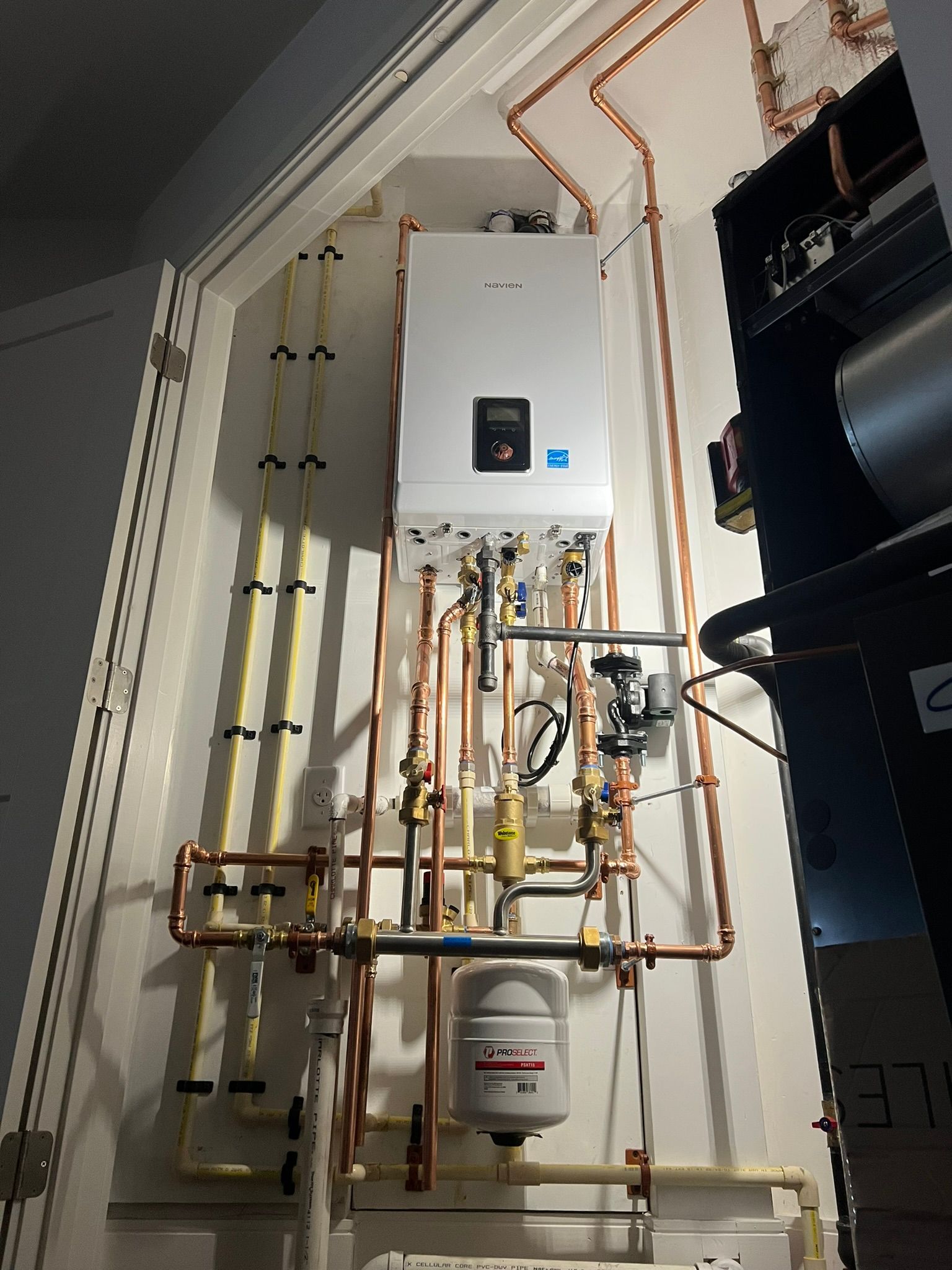 a white boiler is hanging on a wall next to copper pipes