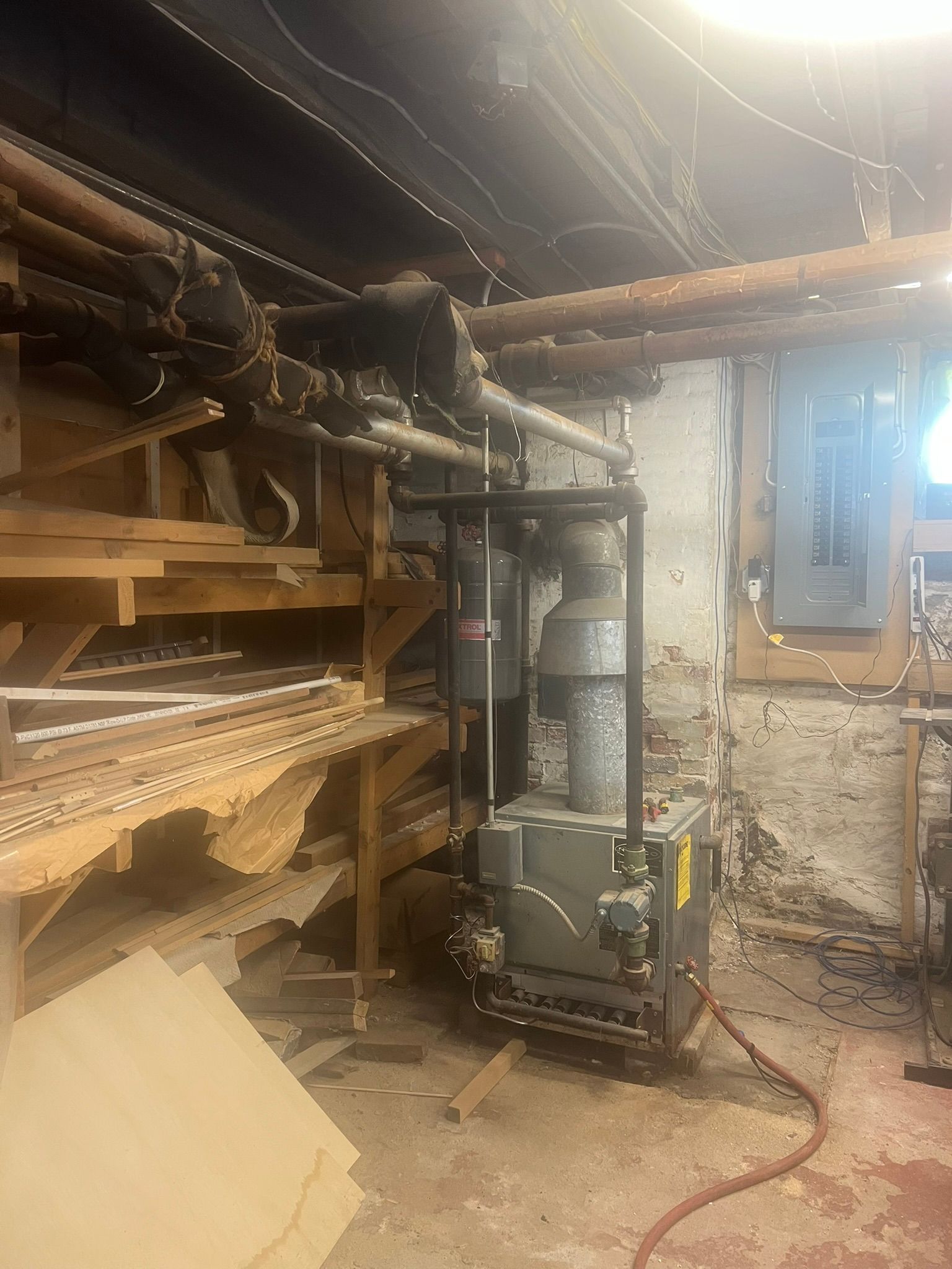 a boiler is sitting in a basement surrounded by wooden shelves and pipes