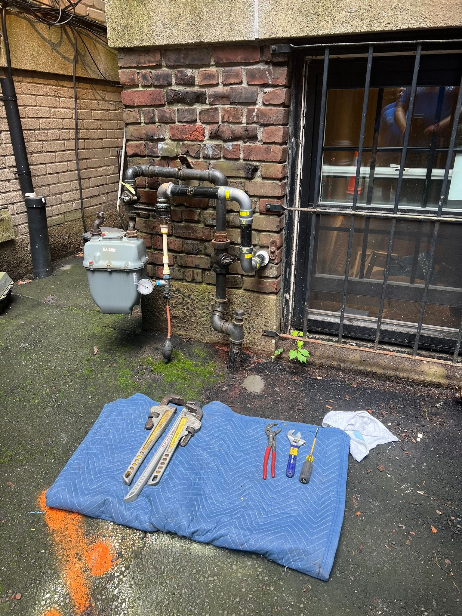 a gas meter is sitting on the ground next to a brick wall