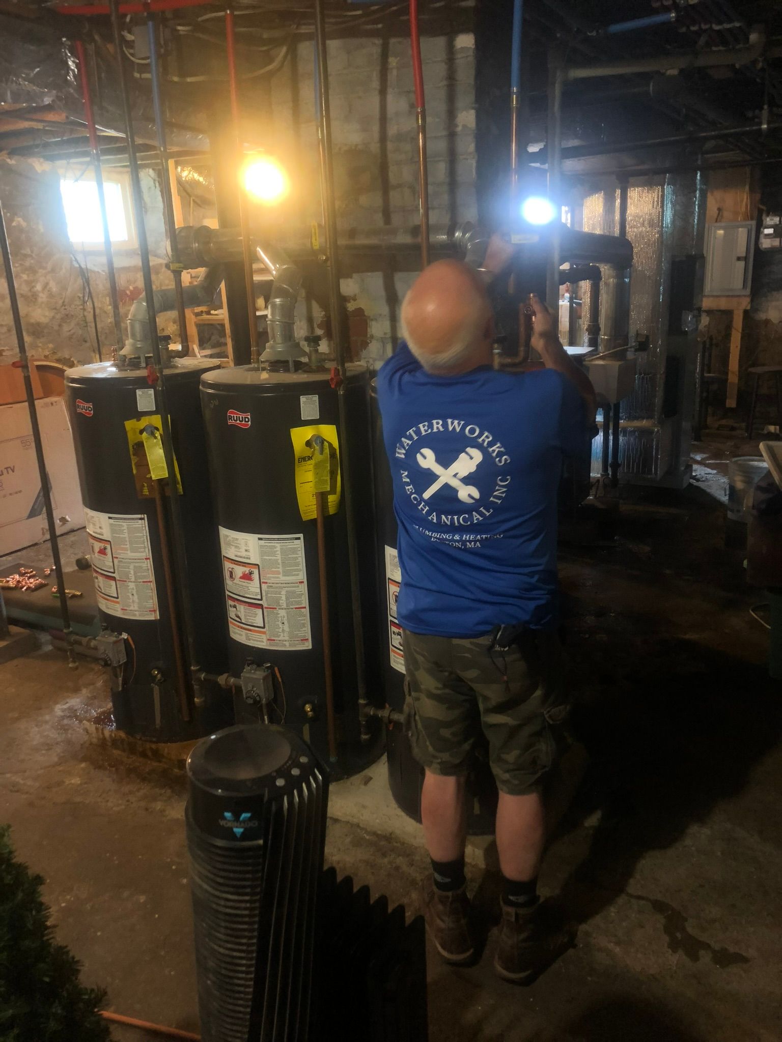 a man in a blue shirt is working on a water heater in a basement