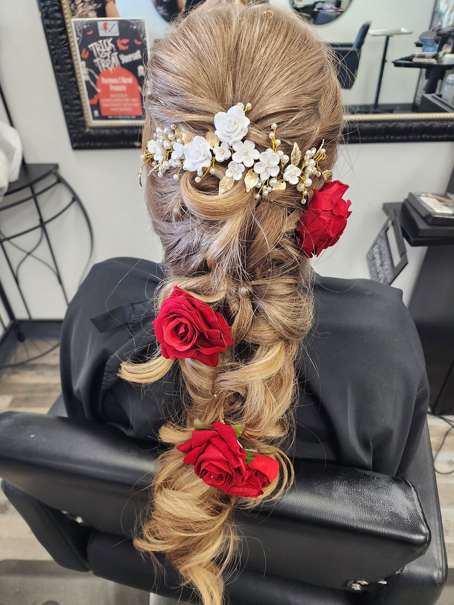 A woman is sitting in a chair with her hair in a braid and flowers in her hair.
