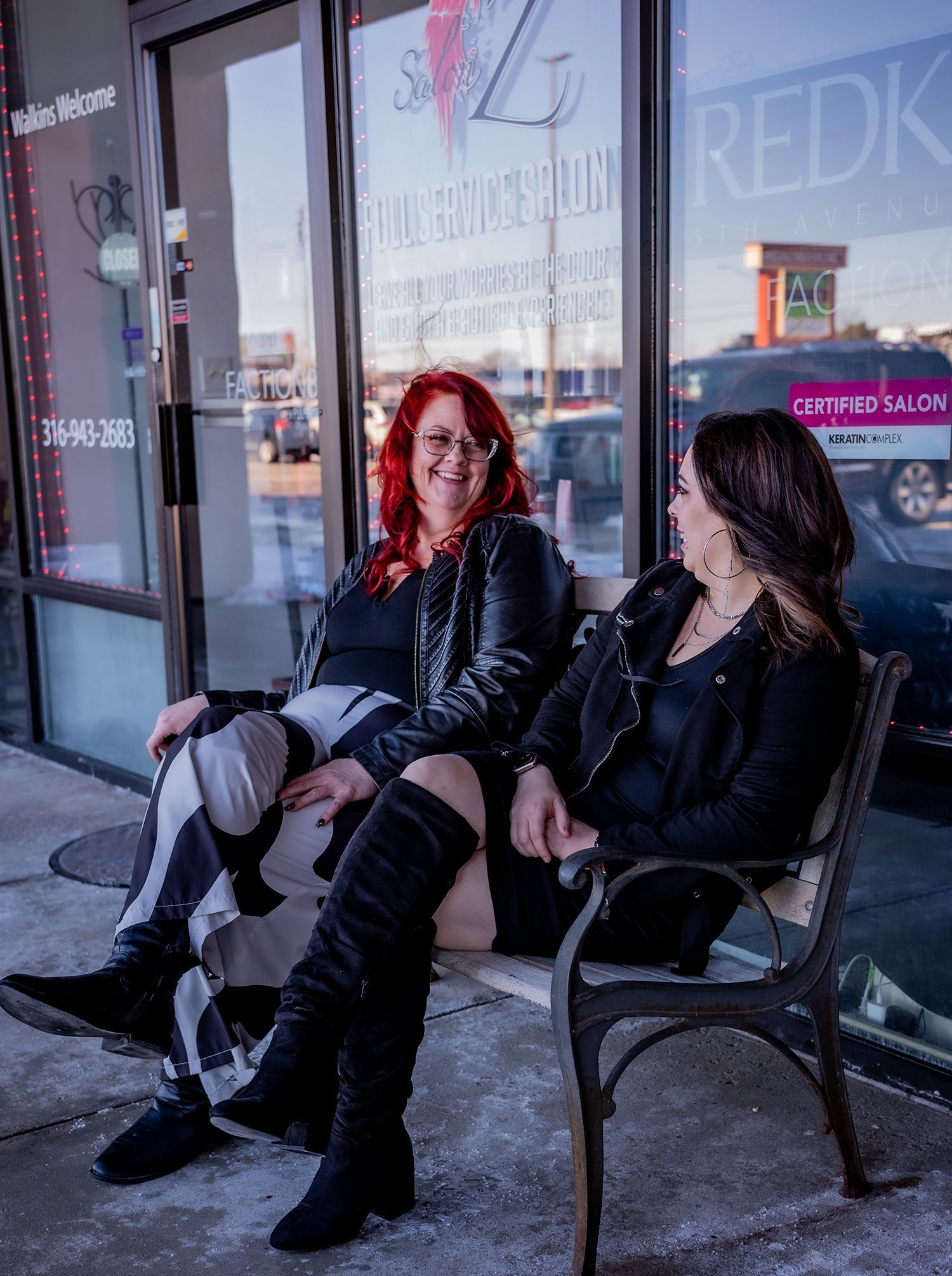 Two women are sitting on a bench in front of a building.