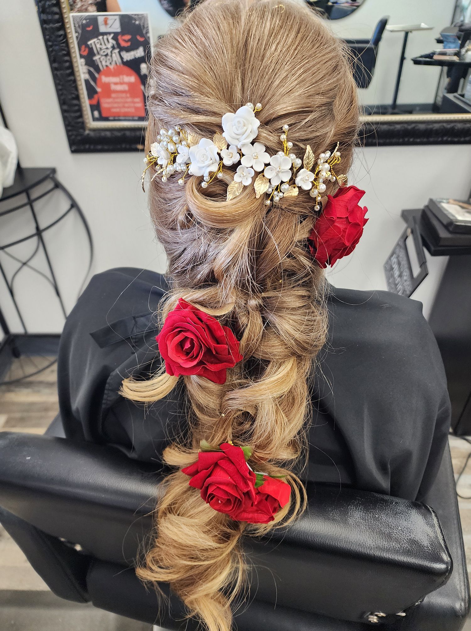 A woman is sitting in a chair with her hair in a braid and flowers in her hair.