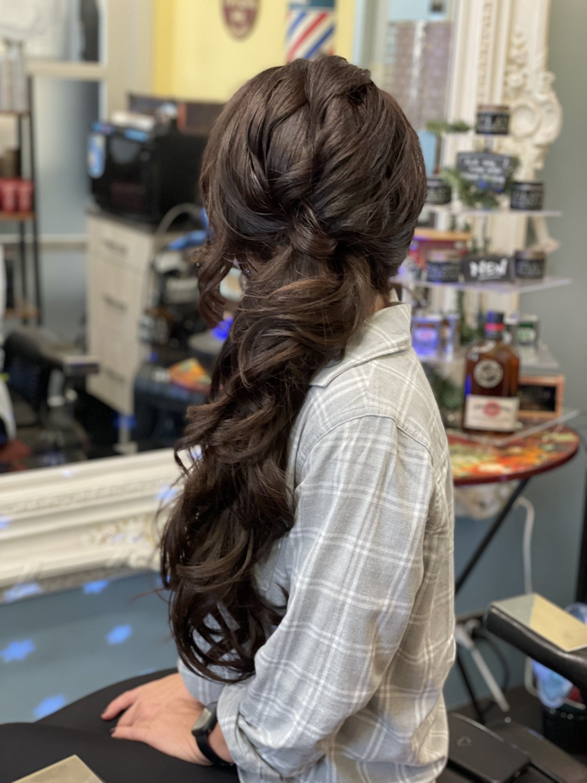 Woman with long, dark, wavy hair styled in an elaborate side braid inside a salon.