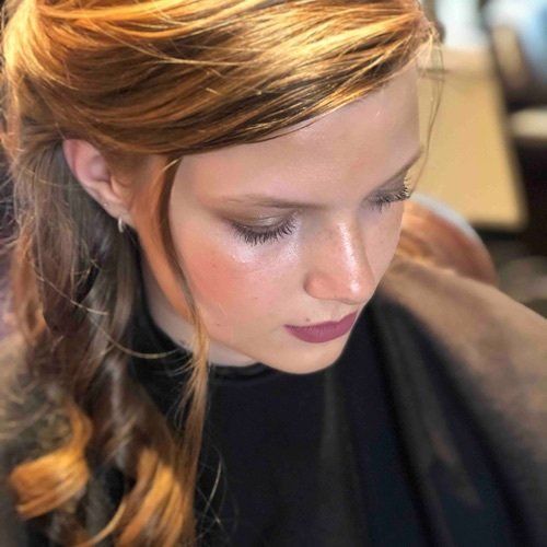 Woman with light skin and reddish-brown hair, wearing makeup, looking down.