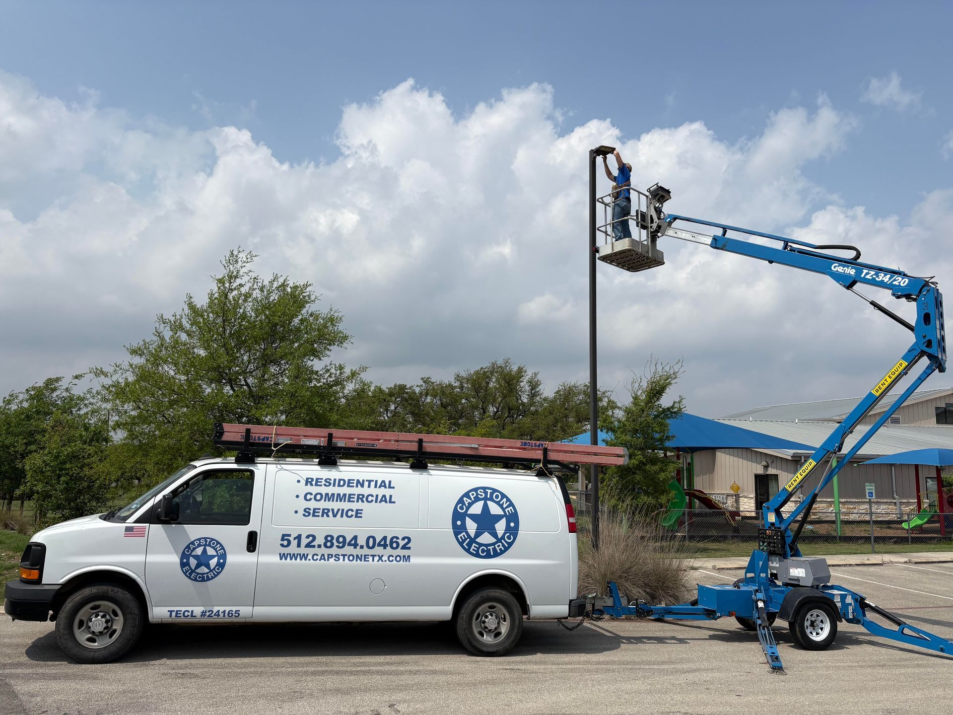 White van with logo and attached blue lift working on a streetlight outdoors.