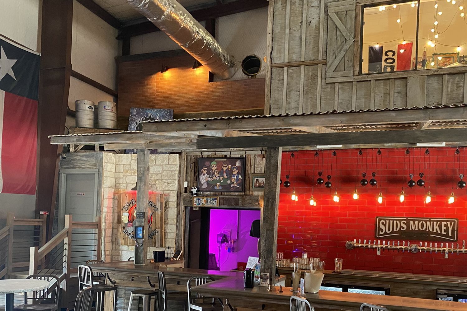 Interior of Suds Monkey brewery in Texas; bar, brick wall, Texas flag, lights.