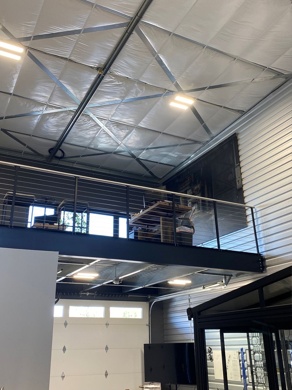 Mezzanine level inside a modern industrial-style building with a reflective ceiling and garage door.