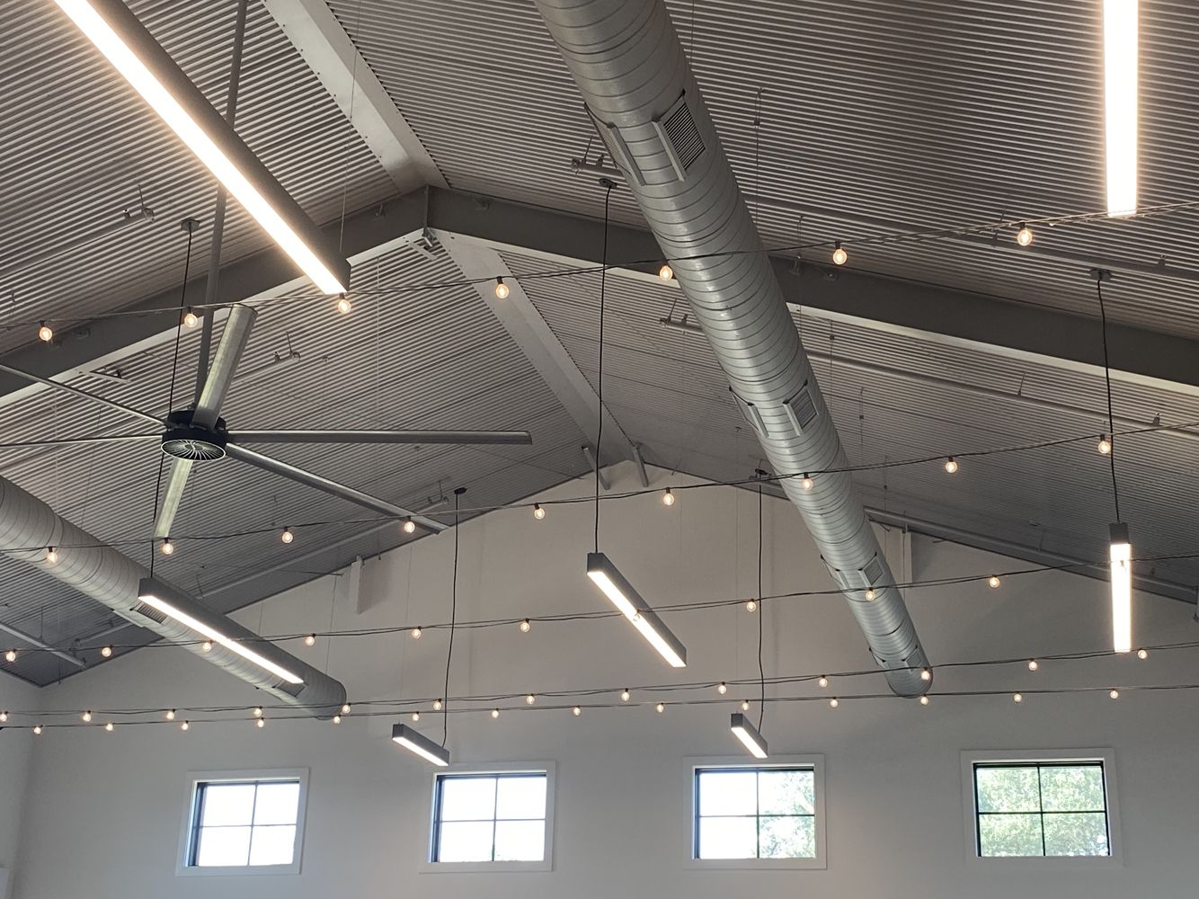 Indoor venue with corrugated metal ceiling, string lights, fluorescent lights, windows.