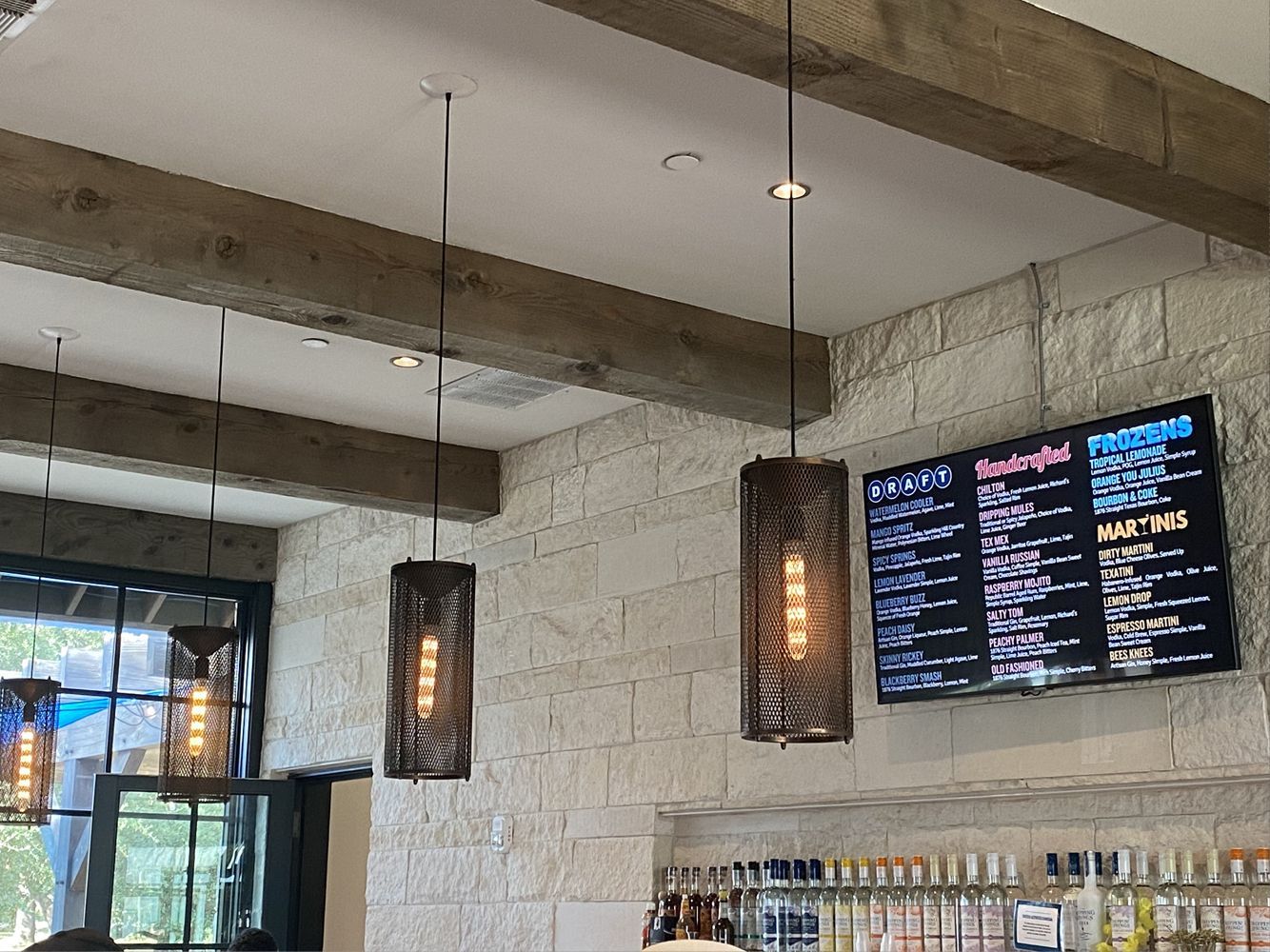 Restaurant interior with textured stone walls, hanging lights, wooden beams, and a menu on a screen.