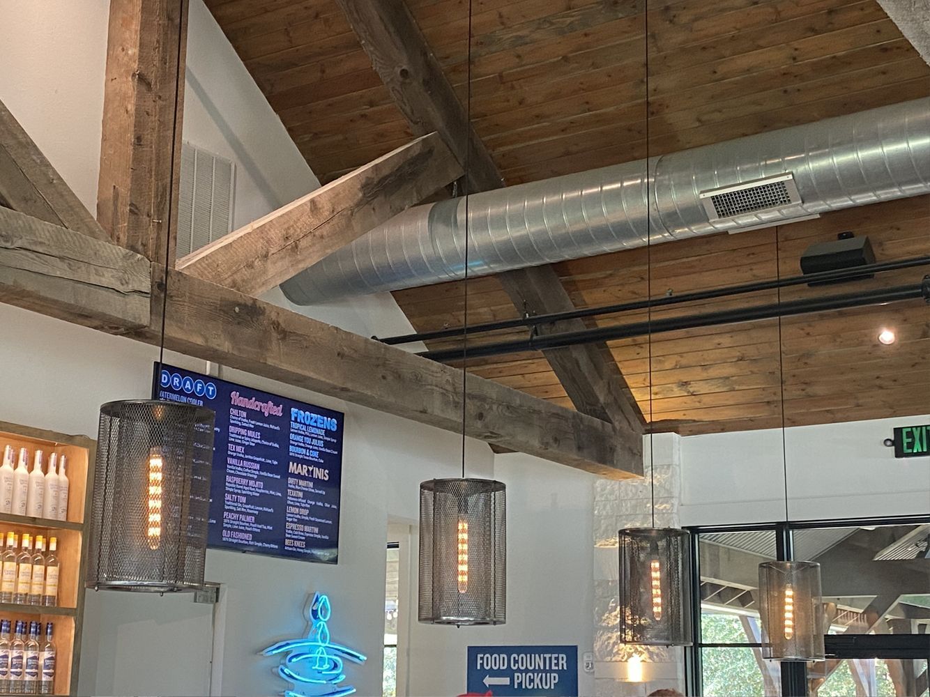 Interior view of a restaurant with wooden beams, hanging lights, and a menu board.
