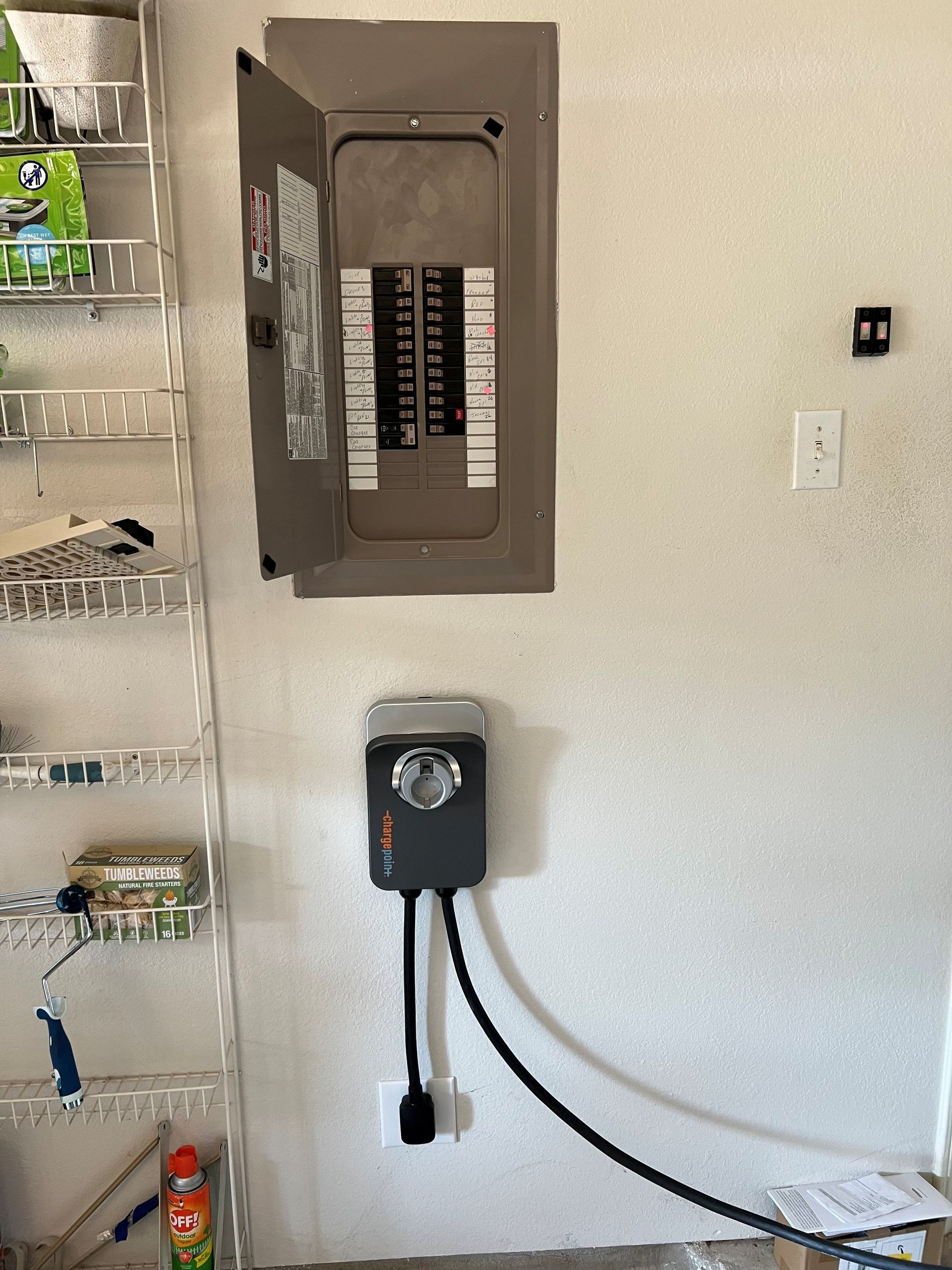 Electrical panel and EV charger mounted on a white wall in a garage setting.
